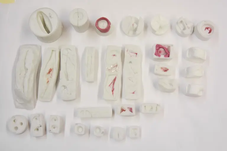 Die Abbildung zeigt eine Vielzahl von Formen aus hellweißem Material, einige mit roten Akzenten. Die Formen sind in unterschiedlichen Größen und Anordnungen angeordnet, darunter ovale, rechteckige und runde Elemente, die scheinbar für künstlerische oder technische Zwecke gestaltet sind.