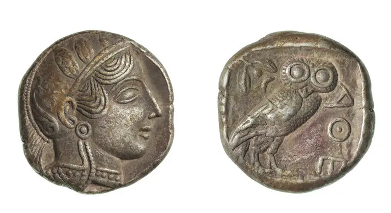Eine antike Münze zeigt auf der Vorderseite das Profil einer Frau mit einer Haarfrisur. Die Rückseite zeigt eine Eule, ein häufiges Symbol der Weisheit, neben weiteren Zeichen.
