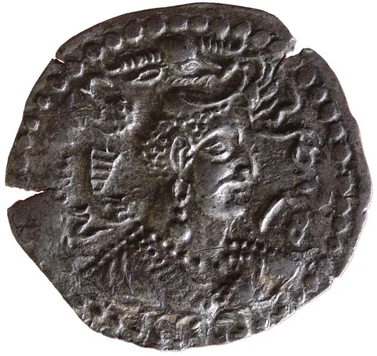 Die Abbildung zeigt eine antike Münze, auf der das Porträt einer Frau mit auffälligen Ohrringen und einer komplexen Frisur zu sehen ist. Im Hintergrund sind weitere kleine Figuren oder Symbole eingraviert, die die Münze zusätzlich verzieren.