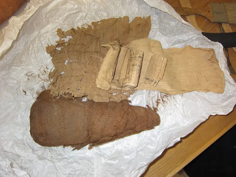 Auf dem Bild sind mehrere Stücke von antikem Papier und Textilien zu sehen, die auf einem weißen, zerknitterten Untergrund liegen. Die Materialien sind in verschiedenen Formen gefaltet und scheinen aus natürlichen Materialien gefertigt zu sein.