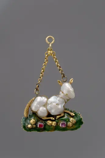 Ein kunstvolles Anhängsel in Form eines stilisierten Pferdes aus Perlen, das auf einer grünen, blattartigen Unterlage sitz. Es sind auch kleine, rote und grüne Edelsteine zu sehen, die das Design schmücken. Der Anhänger hat eine goldene Aufhängung.