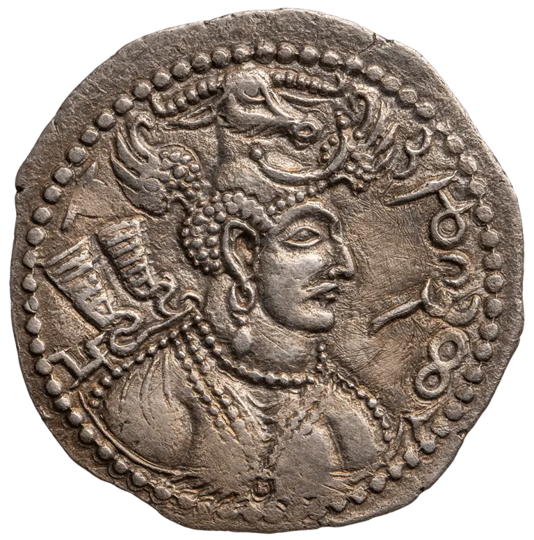 A detailed silver coin featuring a profile of a regal figure adorned with elaborate jewelry and a headdress. The figure holds a flag or sword, with a stylized bull above their head. Decorative beading borders the coin, enhancing its intricate design.