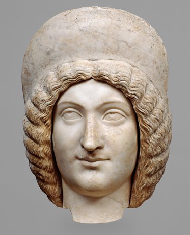 Skulptur eines Kopfes aus Marmor mit lockigem Haar und einem charakteristischen Kopfschmuck. Die Gesichtszüge sind harmonisch und lächelnd, mit klaren Augen und einer sanften Ausstrahlung. Der Hintergrund ist schlicht, um den Fokus auf die Skulptur zu legen.