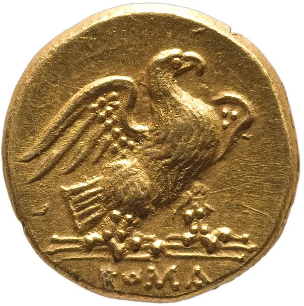 Eine goldene Münze, die einen stilisierten Adler zeigt. Der Adler hat ausgebreitete Flügel und steht auf einer geschwungenen Linie. Unter dem Motiv sind einige floral wirkende Elemente zu erkennen. Die Münze hat eine glatte, glänzende Oberfläche und einen runden Rand.