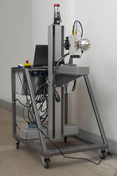 Ein mobiler Forschungsapparat mit einem stabilen Rahmen, ausgestattet mit einer Kamera und einem Steuergerät. An der Unterseite befinden sich Rollen für die Mobilität. Der Apparat ist für wissenschaftliche oder technische Anwendungen konzipiert.