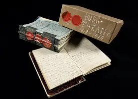 Auf dem Bild sind stapelweise handgeschriebene Notizen und ein beschrifteter Karton zu sehen. Der Karton trägt die Aufschrift „Burg-Theater 1918-1919“. Die Notizen scheinen sich auf das Theater zu beziehen und sind in einem offenen Notizbuch angeordnet.