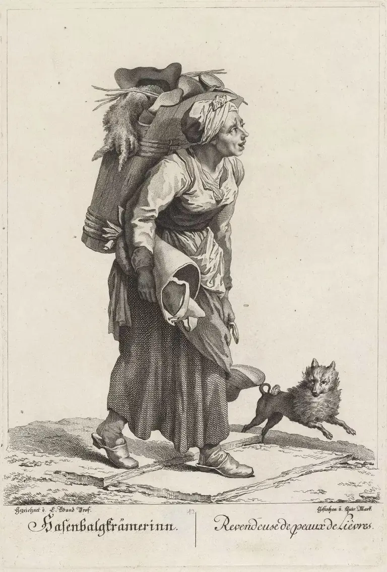 A woman carrying a large bundle on her back stands with a determined expression. She is wearing traditional clothing, and a small dog playfully runs beside her. The scene emphasizes her strength and resilience in a rural setting.