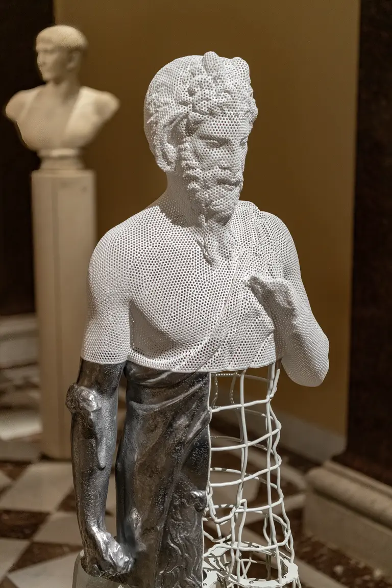 Eine Skulptur eines männlichen Körpers, der teilweise aus einer filigranen netzartigen Struktur besteht. Der Kopf und die Arme sind detailliert ausgearbeitet, während der untere Teil durch ein Gitter ersetzt ist. Die Statue steht in einer musealen Umgebung.