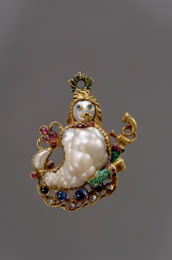 Ein kunstvoller Anhänger in Form einer Meerjungfrau, aus Perlen, Gold und bunten Edelsteinen. Die Meerjungfrau hat geschwungenes Haar, trägt eine Krone und hält ein Musikinstrument. Die Details sind filigran ausgearbeitet und verleihen dem Schmuckstück einen eleganten, fantasievollen Charakter.