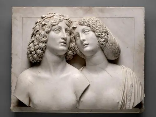 A white marble relief depicts two figures closely positioned, a young man with curly hair adorned with leaves and a woman with smooth, wavy hair. They both have thoughtful expressions, showcasing intricate details in their facial features and clothing, emphasizing an intimate connection between them.