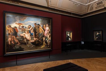 Ein Innenraum eines Museums mit einem großen Gemälde, das mythologische Figuren darstellt. Im Hintergrund sind kleinere Portraits an der Wand zu sehen. Der Boden ist aus Holz und der Raum hat eine elegante Decke.