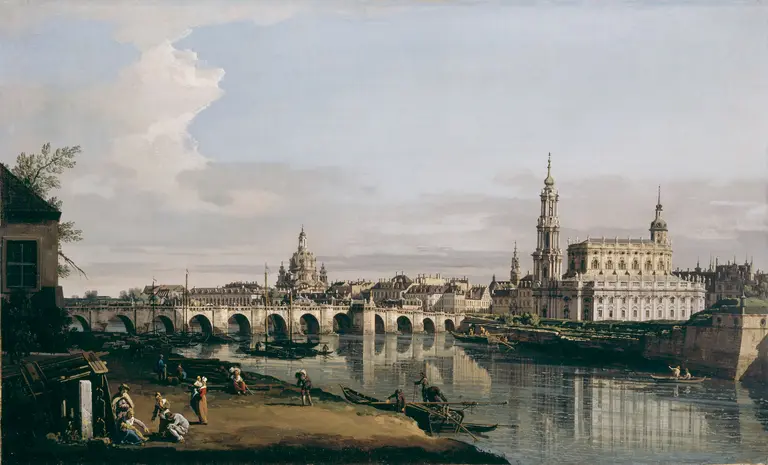 A panoramic view of a riverside city, featuring arched bridges and grand architectural structures, including spires and domes. People are seen along the riverbank and in boats, with a calm river reflecting the buildings under a partly cloudy sky.