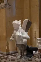 Die Skulptur zeigt eine geflügelte Figur, die eine andere Figur trägt. Die Materialien sind teilweise transparent, wodurch eine interessante Lichtdurchlässigkeit entsteht. Die Darstellung vermittelt Dynamik und Bewegung in einem klassischen architektonischen Hintergrund.