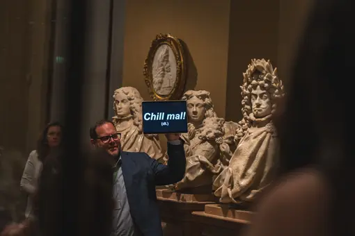 A museum guide holds up a sign reading in front of sculptures in the Kunstkammer of the Kunsthistorisches Museum during a guided tour. 