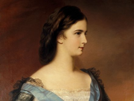 Ein Porträt einer jungen Frau im Profil, mit dunklen, lockigen Haaren und einem eleganten Kleid. Das Kleid ist mit einer blauen Schleife geschmückt, und der Hintergrund ist in warmen, weichen Farbtönen gehalten. Die Pose strahlt Anmut und Würde aus.