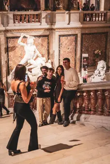 A group of four friends poses for a photo on the staircase of the Kunsthistorisches Museum, with Antonio Canovas impressive sculpture 
