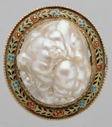 Ein ovaler Reliquienbehälter mit einer großen, glänzenden Perle in der Mitte, umgeben von einer Verzierung aus buntem Emaille mit floralem Muster in Blau, Rot und Grün. Die Perle hat eine ungewöhnliche, natürliche Form.