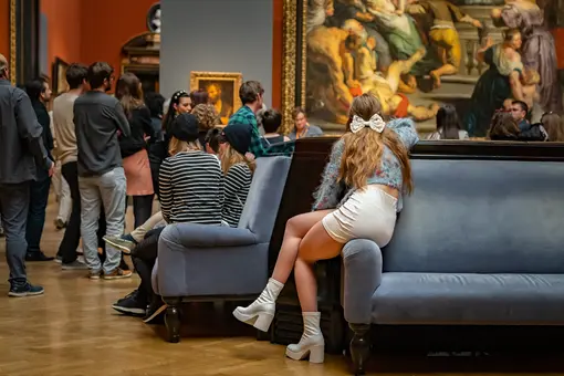 A group of people stands in the Picture Gallery observing several artworks.