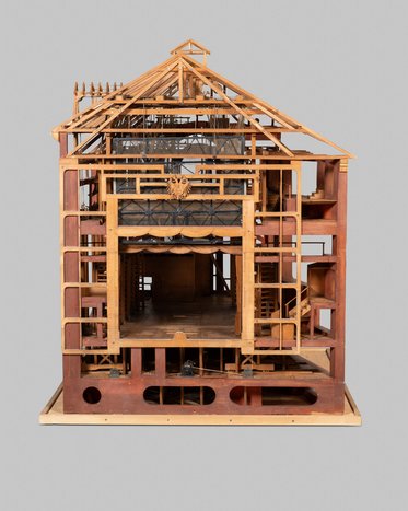 Ein Modell eines Hauses mit einem offenen Grundriss. Deutliche architektonische Details sind sichtbar, darunter Treppen, Fenster und ein Dachstuhl. Die Struktur ist aus Holz und zeigt mehrere Etagen. Die Innenräume sind deutlich erkennbar, was einen Einblick in die Raumaufteilung ermöglicht.