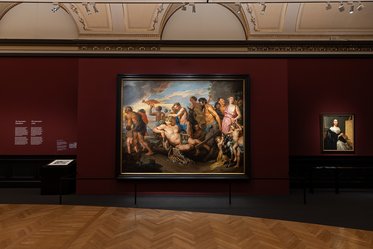 Im Bild ist ein Gemälde in einem Museum zu sehen, das eine dramatische Szene mit mehreren Figuren darstellt. Die Wände sind rot gestrichen, und das Gemälde wird in einem Rahmen präsentiert. Rechts davon hängt ein weiteres kleines Porträt an der Wand.