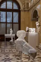 Im Bild sind verschiedene Skulpturen in einem Museum zu sehen. Eine der Skulpturen ist aus Drahtgeflecht und zeigt die Form eines menschlichen Körpers. Weitere Arbeiten, darunter eine Statue und eine Reliefdarstellung, sind ebenfalls in der Galerie ausgestellt.