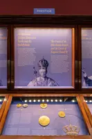 Ein Vitrinenbereich zeigt die Krone des Heiligen Römischen Reiches und die Krone von Kaiser Rudolf II. Im Hintergrund stehen Informationen über die historischen Bedeutung dieser Kronen. Unterhalb sind verschiedene Medaillen und Münzen ausgestellt, die zur Thematik passen.