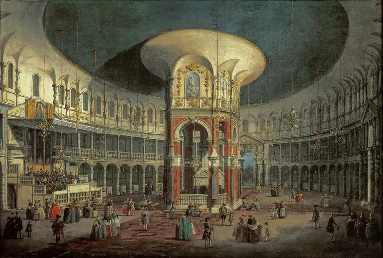 A grand interior of a circular building, featuring a large, ornate central structure and a high ceiling. People dressed in historical garments gather in the space, with balconies lining the walls and decorations adding to the opulence. The atmosphere suggests a festive or ceremonial event.