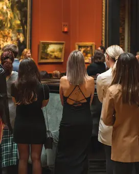 A group of people stands in the Picture Gallery observing several artworks.