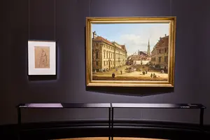 Ein Ausstellungsraum mit zwei Kunstwerken: Links ein gerahmtes Blatt mit einer Zeichnung und rechts ein großes Gemälde eines Stadtbildes, das Menschen und Gebäude zeigt. Der Raum hat dunkle Wände und eine elegante Präsentation.