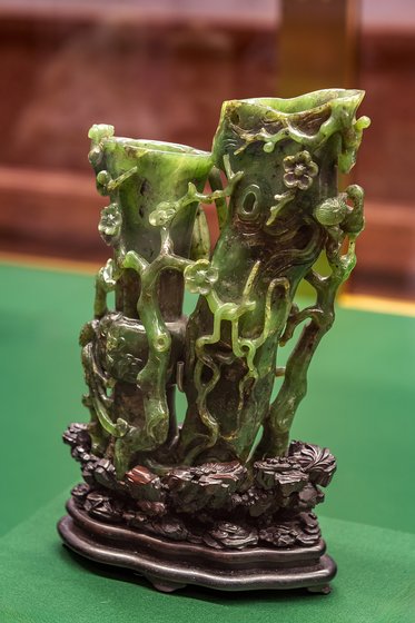 Eine detaillierte Skulptur aus grünem Jade, die zwei stilisierte Bambusstäbe darstellt, umgeben von feinen Blatt- und Blumenmotiven. Die Skulptur steht auf einer verzierter Basis und vermittelt eine harmonische Verbindung zur Natur.