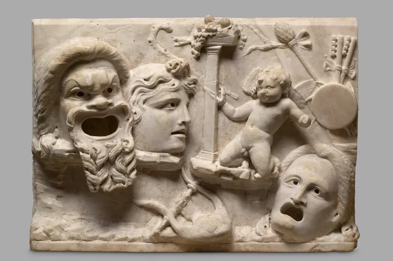 Relief aus Marmor, das drei Gesichter zeigt: einen bärtigen Mann mit einem offenen Mund, eine weibliche Figur mit einer neutralen Mimik und ein kindliches Wesen, das fröhlich wirkt. Das Arrangement ist in antikem, dramatischem Stil gestaltet und enthält mythologische Elemente.