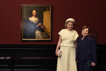 Zwei Frauen stehen lächelnd vor einem großformatigen Porträt in einem Museum. Das Bild zeigt eine Frau in historischer Kleidung. Die Wände sind dunkelrot, und der Rahmen des Porträts ist goldfarben.