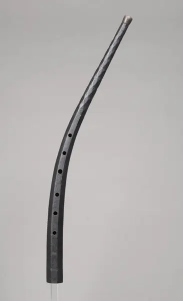 Eine gebogene Röhre aus schwarzem Material, die mehrere Löcher aufweist. Der obere Teil endet mit einer abgerundeten Spitze. Die Form und das Material deuten darauf hin, dass es sich möglicherweise um ein Musikinstrument oder ein dekoratives Objekt handelt.