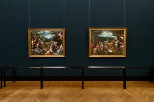 Zwei Gemälde hängen an einer dunkelblauen Wand in einem Museum. Das linke Bild zeigt eine lebhafte Szene mit Menschen und Tieren in einer ländlichen Umgebung. Das rechte Bild zeigt ebenfalls eine ländliche Szene mit arbeitenden Menschen, Obst und weiteren Details, die das ländliche Leben darstellen.