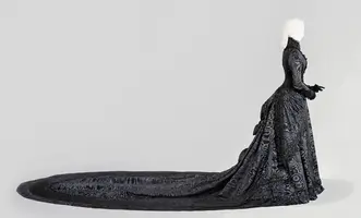 Eine lange, schwarze Robe aus aufwendigem Stoff, die sich bis zum Boden erstreckt. Die Figur trägt die Robe mit einem eleganten Schnitt und einem trächtigen Zug, während das Design durch filigrane Muster verziert ist. Die Silhouette hat blondes, glattes Haar.