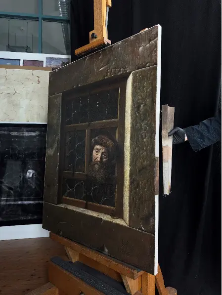 A painting depicts a bearded man looking out of a barred window. It stands on an easel during restoration.