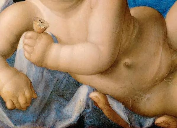 Das Bild zeigt einen Teil eines nackten Babys, das in weichen Stoffen gebettet ist. Es hält eine kleine Glocke in der Hand. Im Hintergrund ist eine sanfte, blaue Wand zu sehen, die den Fokus auf das Kind lenkt.