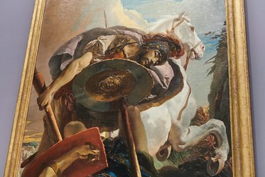 Eine historische Malerei zeigt einen Krieger, der einen Helm und ein Schild trägt. Im Hintergrund sieht man ein Pferd und eine malerische Landschaft. Der Krieger ist in einer dynamischen Pose, während das Pferd einen ruhigen Ausdruck hat.