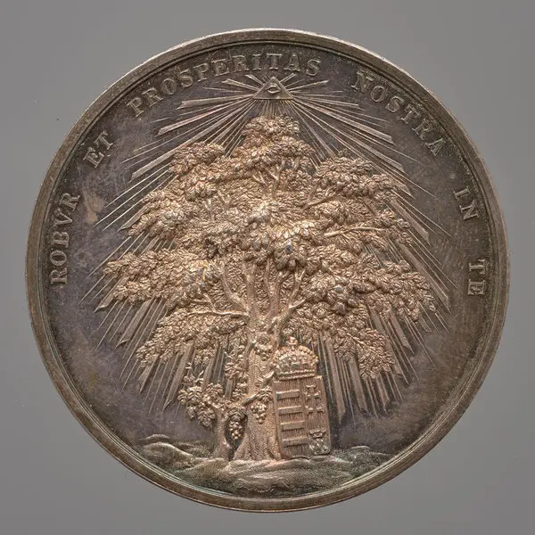 Eine Medaille zeigt einen reich verzweigten Baum, der von Sonnenstrahlen umgeben ist. Unter dem Baum sind zwei Figuren, und im Hintergrund ist ein Gebäude angedeutet. Die Inschrift lautet „Robur et prosperitas nostra in te“.