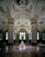 Ein prächtiger Innenraum eines Museums mit hohen Decken und kunstvollen Verzierungen. In der Mitte steht eine Statue auf einem Sockel, umgeben von historischen Objekten in Vitrinen. Die Wände sind in sanften Farben gehalten und Fenster lassen natürliches Licht herein.