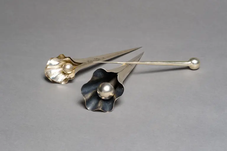 Three metallic flower-shaped objects are displayed on a gray background. Two are pointed and feature a rounded center, while the third is elongated and smooth. The design highlights a combination of shiny and matte finishes, emphasizing their artistic craftsmanship.
