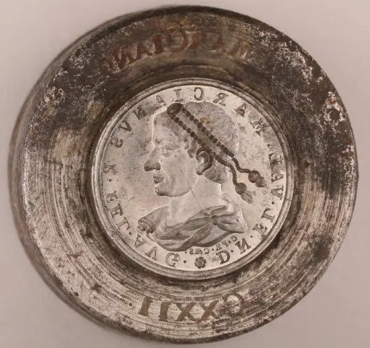 Das Bild zeigt eine alte Münze mit dem Portrait eines Mannes im Profil. Der Mann trägt einen Zopf und schaut nach links. Um das Portrait sind Inschriften angebracht, wahrscheinlich mit seinem Namen und Titel. Der Münzrand ist abgenutzt und zeigt Gebrauchsspuren.