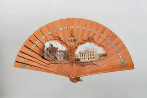 Ein handgefertigter Fächer aus Holz mit zwei bemalten Szenen, die Architektur darstellen. In der Mitte befindet sich eine stilisierte Blütenampel, umgeben von feinen Verzierungen. Der Fächer hat einen soliden Griff und elegante Details, die seine kunstvolle Gestaltung betonen.