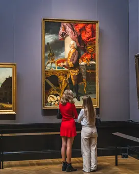 Two visitors observe a large painting in the Picture Gallery of the Kunsthistorisches Museum.