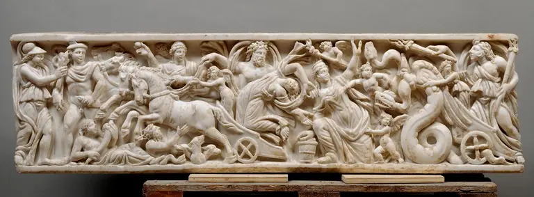 The image depicts a detailed marble relief depicting a dynamic scene with multiple figures interacting, including warriors, mythical beings, and flowing drapery. The composition includes horses, a chariot, and elements of conflict, capturing a moment of action and storytelling from ancient mythology.