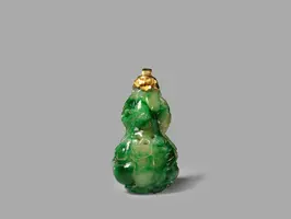 Eine grüne Jade-Flasche in Form einer stilisierten Vase mit detaillierter Oberfläche und goldener Kappe. Die Flasche zeigt geschwungene Linien und ein organisches Design, das die natürliche Textur von Jade betont.