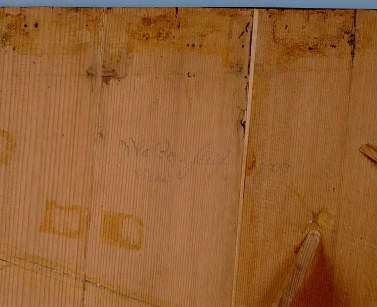 Eine gepflasterte Fläche aus Holz mit sichtbaren Flecken zeigt die handschriftliche Notiz 