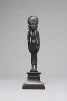 Bronzes Statue einer weiblichen Figur mit einem großen, runden Kopf und einer kleinen Brust. Sie hat lange Arme und steht auf einem rechteckigen Sockel. Die Statue zeigt kunstvolle Details und ist aus einem patinierten Material gefertigt.