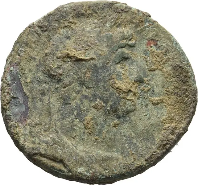Eine antike Münze mit einer erkennbaren, aber verwitterten Darstellung eines menschlichen Gesichts auf der Vorderseite. Die Münze zeigt starke Abnutzungserscheinungen und hat eine unebene, grüne Patina.