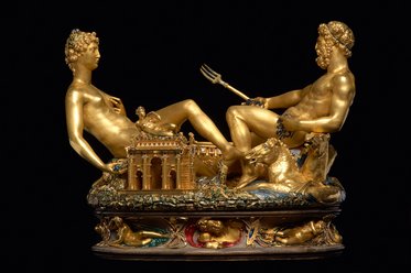 Eine goldene Skulptur zeigt zwei männliche Figuren, die entspannt nebeneinander sitzen. Der eine hält einen Dreizack, während der andere eine entspannte Pose einnimmt. Im Hintergrund befindet sich ein architektonisches Element, das als Tempel interpretiert werden kann. Die gesamte Komposition strahlt eine luxuriöse und kunstvolle Ästhetik aus.